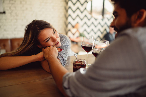 Romantic couple sitting in cafe and drinking red wine. Attractive girl holding her boyfriend hand and looking at him. - 写真・画像
