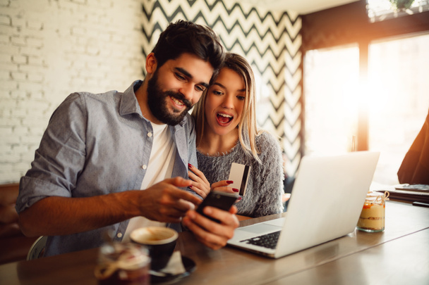 Молодая пара делает покупки онлайн в кафе. Человек проверяет свой банковский счет
. - Фото, изображение