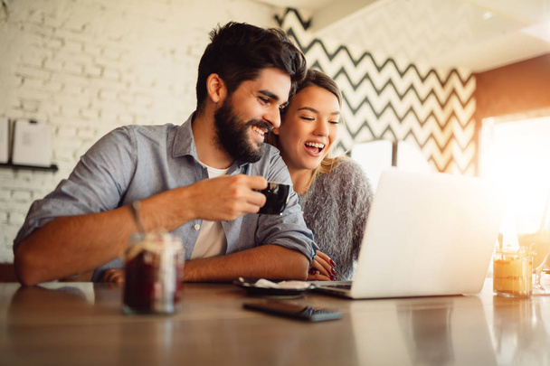 Ευτυχισμένο ζευγάρι σερφ σε ένα φορητό υπολογιστή στο café. Ψώνια online ή βίντεο συνομιλία ζευγάρι. - Φωτογραφία, εικόνα