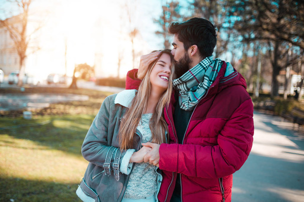 schöner Mann küsst seine Freundin auf die Stirn, wenn sie im Park spazieren gehen und den Valentinstag feiern. - Foto, Bild
