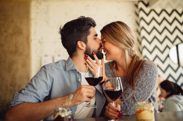 Handsome man kissing his girlfriend in nose. Couple drinking wine a cafe and celebrating Valentine's day. - 写真・画像