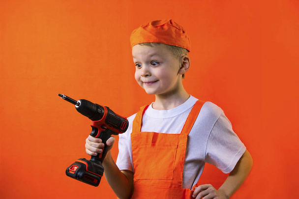 funny builder boy holding a screwdriver on an orange background - Фото, зображення