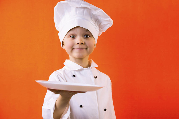 funny boy chef cook holding a plate for dough on an orange background - Foto, afbeelding