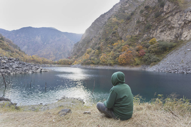 Un homme vêtu d'une veste verte est assis au bord du lac
 - Photo, image