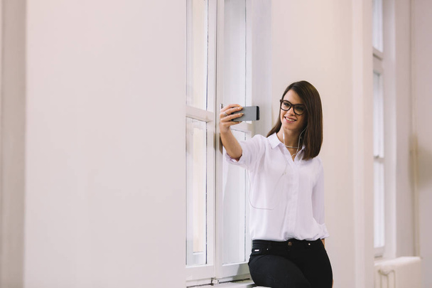Mujer de negocios haciendo selfie, escuchando la música o video chat en la oficina
. - Foto, Imagen