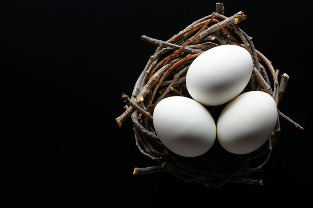 Easter background. White eggs in a nest from branches on black background - Photo, image