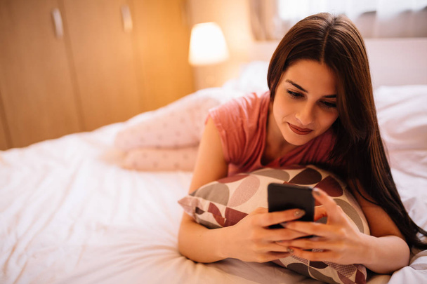 Joven chica atractiva acostado en la cama y el uso de móvil
 - Foto, imagen