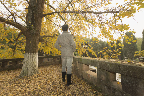 Чоловік у довгих чоботях стояв під золотим високим деревом гінкго - Фото, зображення