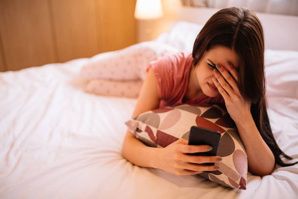 Joven chica atractiva acostado en la cama y el uso de móvil
 - Foto, Imagen
