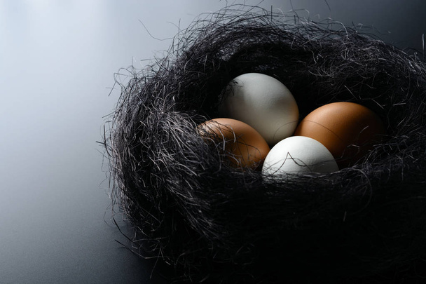 Biały i brązowy jaja w gnieździe z sizalu na czarnym tle - Zdjęcie, obraz