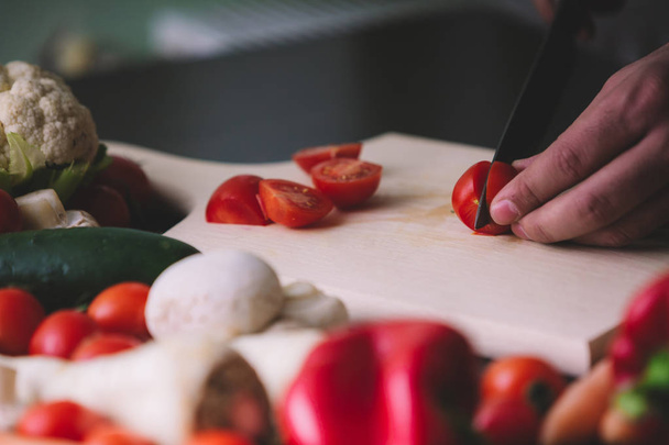 Close-up de mãos de homem ao cortar tomates cereja em tábua de madeira
. - Foto, Imagem