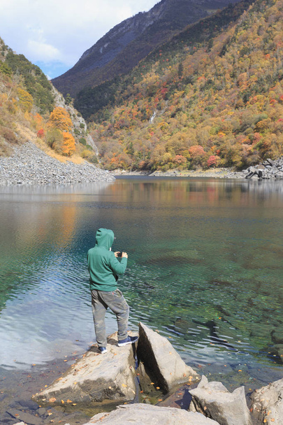 Un hombre está de pie junto al lago y tomando fotos
 - Foto, imagen