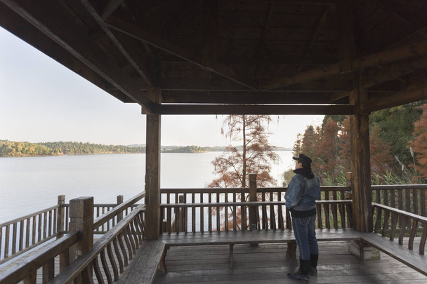 Um homem asiático de pé em um pavilhão de madeira com vista para um distante
 - Foto, Imagem