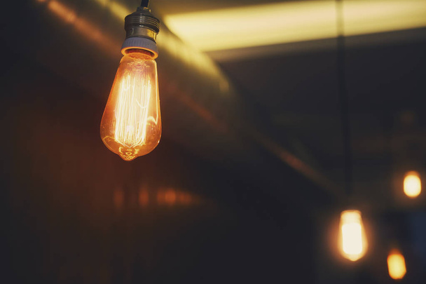 Světlé teplé oranžové svítidlo Edison na tmavém pozadí. Jemné zpracování a tónování fotografií. Vintage žárovka visí na kabel. - Fotografie, Obrázek