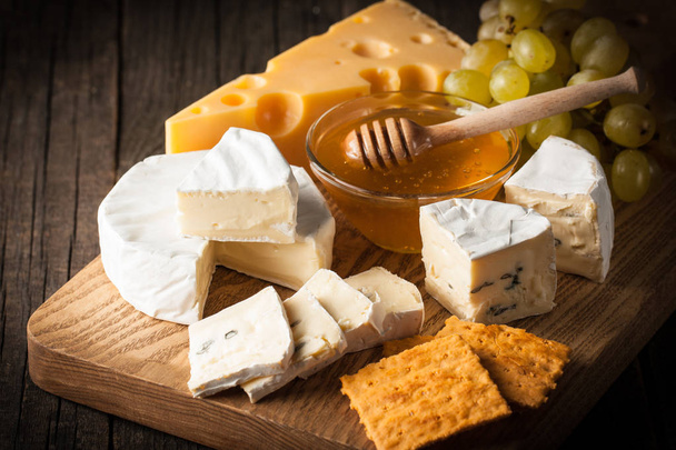 Slate board with various cheese and a glass of red rose wine. Brie. Camembert. Gouda, Masdaam, Roquefort, Cheddar and grapes on a wood with nuts, honey, crackers, blue cheese. Italian, French cheese. - Photo, Image