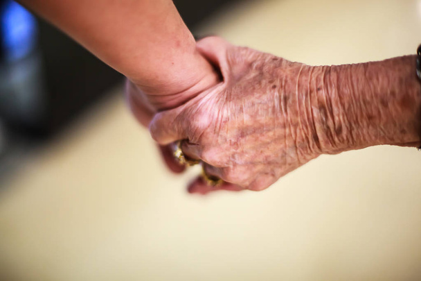 gerimpeld bejaarde vrouw hand hebt aan jonge man hand, wandelen in winkelcentrum. Familie relatie, gezondheid, hulp, ondersteuning, verzekering concept. - Foto, afbeelding