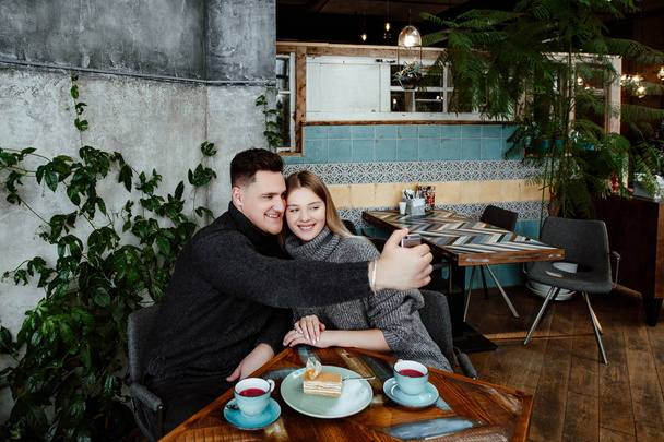 Joven hermosa pareja amorosa en la cafetería. El hombre y la mujer toman una selfie, abrazan, toman el té sabroso y comen el postre
. - Foto, imagen