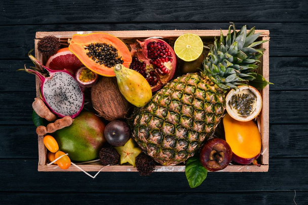 Tropical fruit in a wooden box. Papaya, Dragon Fruit, rambutan, tamarind, cactus fruit, avocado, granadilla, carambola, kumquat, mango, mangosteen, passionfruit, coconut. - Foto, afbeelding