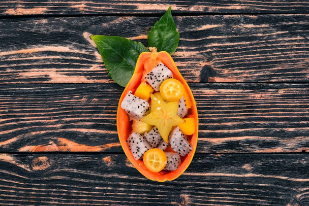 Tropical Fruit Salad Served in half a Papaya. Dragon Fruit, rambutan, tamarind, cactus fruit, avocado, mango. On a wooden background. Top view. - Foto, immagini