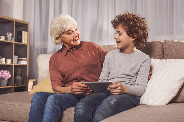 Outgoing grandmother and boy holding electronic tablet - Foto, afbeelding