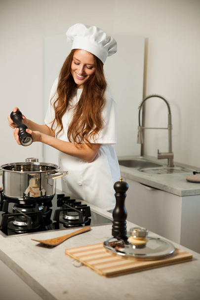 Beautiful young woman in white chef uniform cooking in the kitch - Photo, Image
