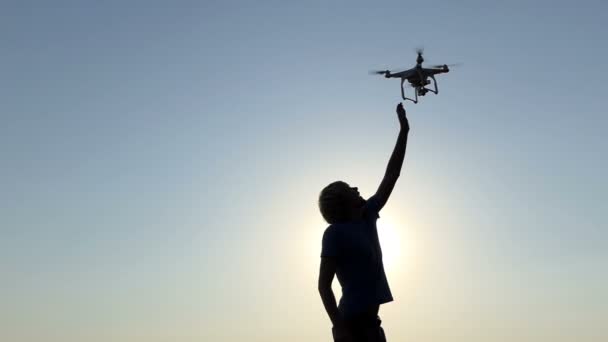 Młody człowiek próbuje dotknąć latający dron o zachodzie słońca w slo-mo - Materiał filmowy, wideo