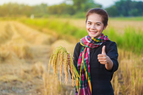 woman showing thumb up and holding rice in field - Photo, Image
