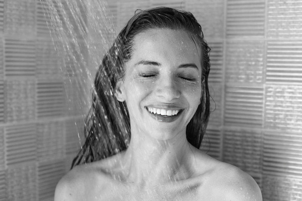 Fotos horizontales en blanco y negro de una joven morena tomando una ducha en el hotel, disfrutando de gotas de agua, divirtiéndose, relajándose después de una dura jornada de trabajo en la oficina. Feliz dama cerrando los ojos del placer
. - Foto, imagen