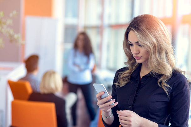 Young attractive businesswoman talking on mobile phone in office, her colleagues on the background - Фото, зображення