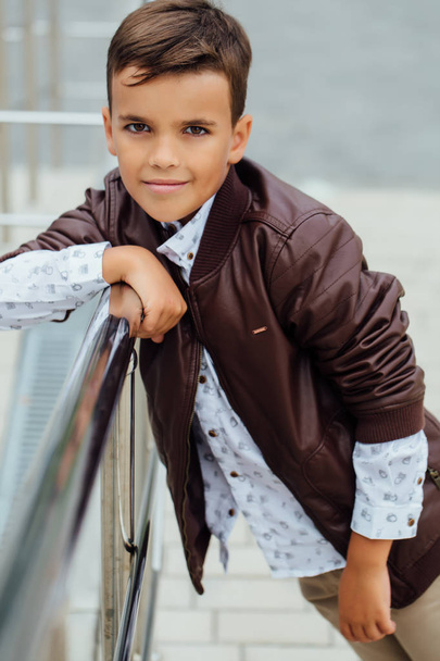 Teenager boy is waiting for the stairs at the railing. Fashionable kid in stylish city clothes. - Photo, Image