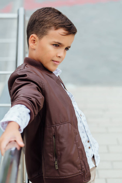 Teenager boy is waiting for the stairs at the railing. Fashionable kid in stylish city clothes. - Foto, immagini