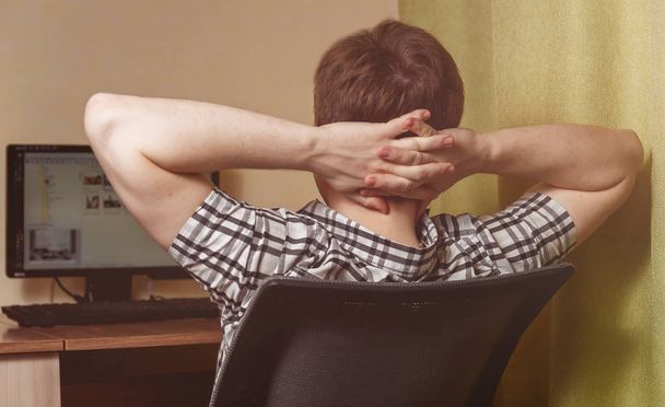 Rear view of man relaxing on chair at home near computer after hardwork - Foto, Bild