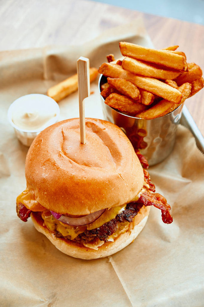 Primer plano de hamburguesa casera servida con papas fritas crujientes y mayonesa en bandeja blanca sobre mesa de madera
 - Foto, imagen