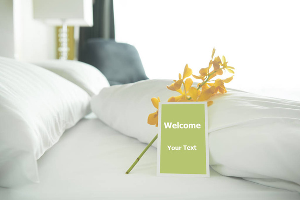 Uvítací karta umístěná v posteli v hotelovém pokoji se žlutou orchidejí. - Fotografie, Obrázek