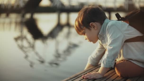 Schattige Europees jongen speelt met meerwater op een pier. Weinig mannelijke kind met rugzak verkennen van de zomer natuur. 4 k close-up. - Video