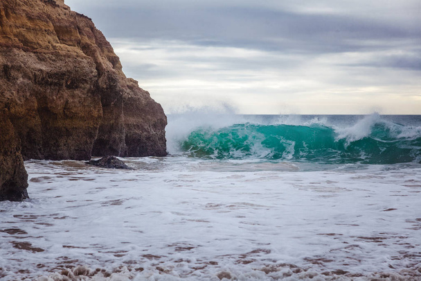 A beautiful bright turquoise wave is broken against the rocks ag - Photo, Image