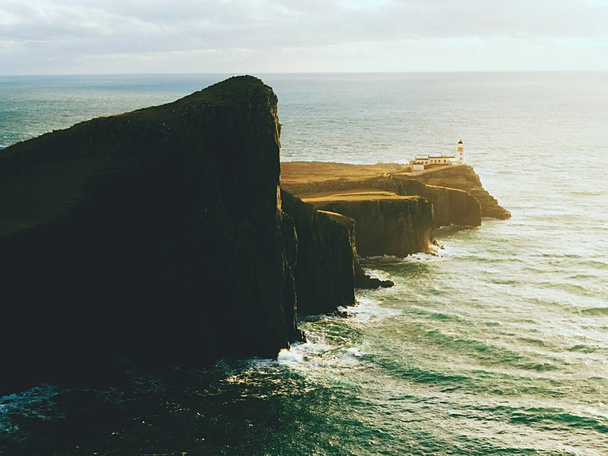 有名な Neist ポイント、スカイ島の岩石の多い海岸の崖の上の灯台を見て - 写真・画像