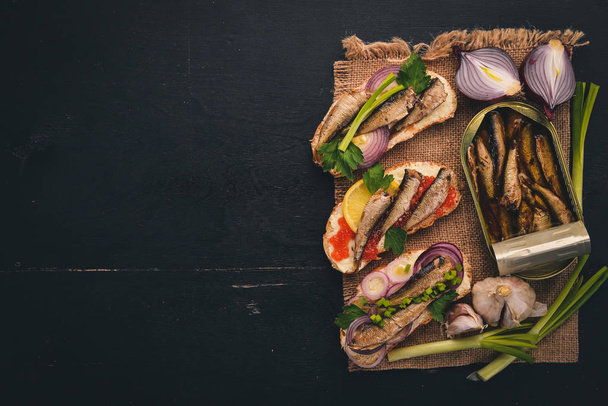 A set of sandwiches with sprats, and caviar, onion and parsley, on a wooden background. Top view. Copy space. - Photo, image