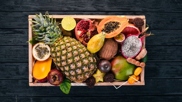 Tropical fruit in a wooden box. Papaya, Dragon Fruit, rambutan, tamarind, cactus fruit, avocado, granadilla, carambola, kumquat, mango, mangosteen, passionfruit, coconut. - Photo, image