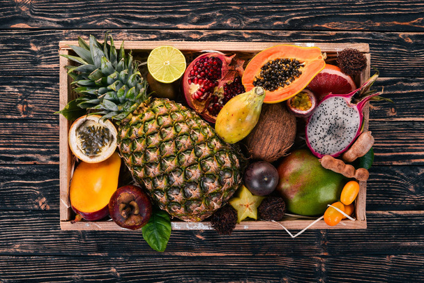 Tropical fruit in a wooden box. Papaya, Dragon Fruit, rambutan, tamarind, cactus fruit, avocado, granadilla, carambola, kumquat, mango, mangosteen, passionfruit, coconut. - Zdjęcie, obraz