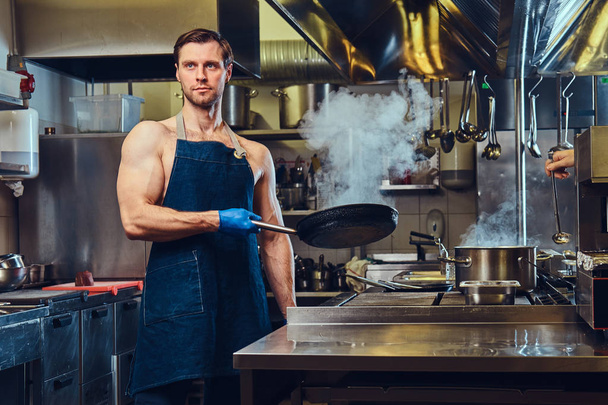 Atletische chef-kok houdt droge pan in een professionele keuken van het hotel. - Foto, afbeelding