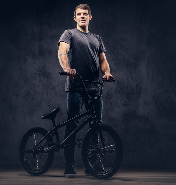 Handsome man in t-shirt and jeans standing with BMX. Isolated on a dark background. - Photo, Image