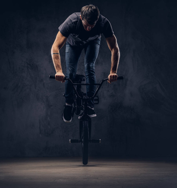 Красивий чоловік у футболці і джинсах робить акробатичну фігуру з BMX в студії
. - Фото, зображення