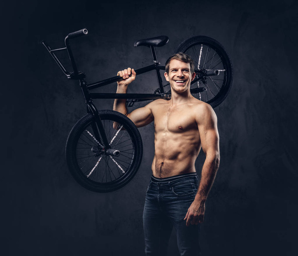 ハンサムな Bmx を持って人を肩に乗せて自転車上半身裸の男の笑みを浮かべてします。暗い背景に分離. - 写真・画像