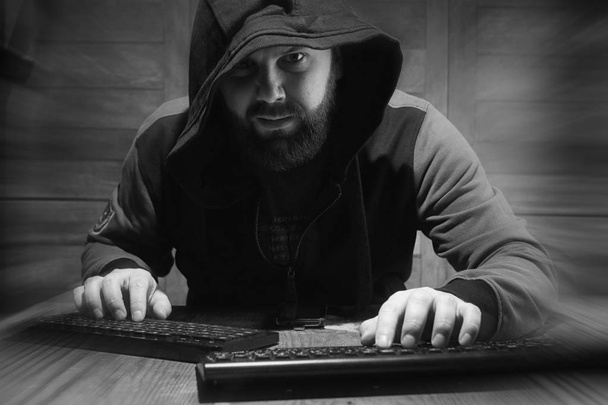 The hacker in the hood sits and works behind the computer - Foto, imagen