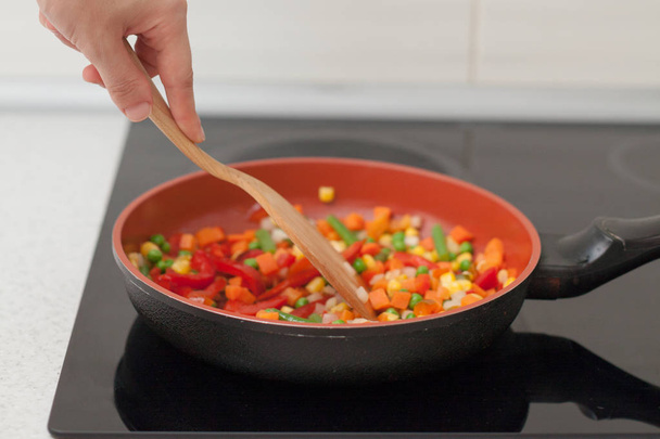 Τα λαχανικά είναι σε ένα τηγάνι. Γυναίκα μαγείρεμα πολύχρωμα φρέσκα λαχανικά για μια ηλεκτρική κουζίνα - Φωτογραφία, εικόνα