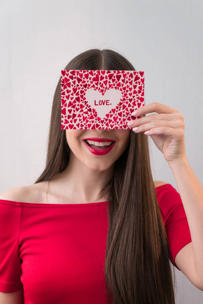 Portrait of a sweet perfect girl smiling at camera with heart shaped paper in her hands. Valentine's Day or Women's Day concept - Photo, Image
