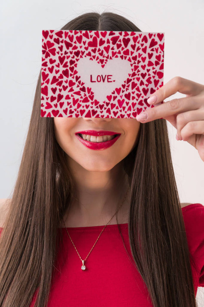 Portrait of a sweet perfect girl smiling at camera with heart shaped paper in her hands. Valentine's Day or Women's Day concept - Foto, afbeelding