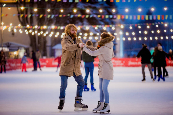 Theme ice skating rink and loving couple. meeting young, stylish people ride by hand in crowd on city skating rink lit by light bulbs and lights. Ice skating in winter for Christmas on ice arena - Foto, afbeelding