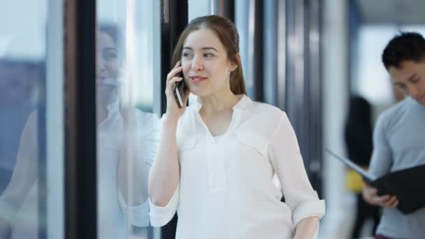 4K businesswoman standing next to window and talking on cell phone in city office - Video, Çekim